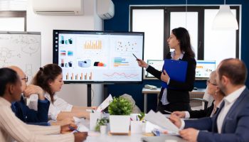young-team-leader-big-corporation-briefing-coworkers-pointing-graph-meeting-corporate-staff (Large)
