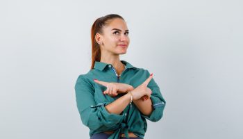 young woman pointing left and right, looking up in green shirt and looking hopeful. front view.